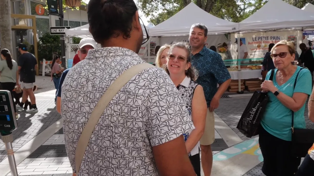 A food tour guide talking with smiling guests at an outdoor market in West Palm Beach